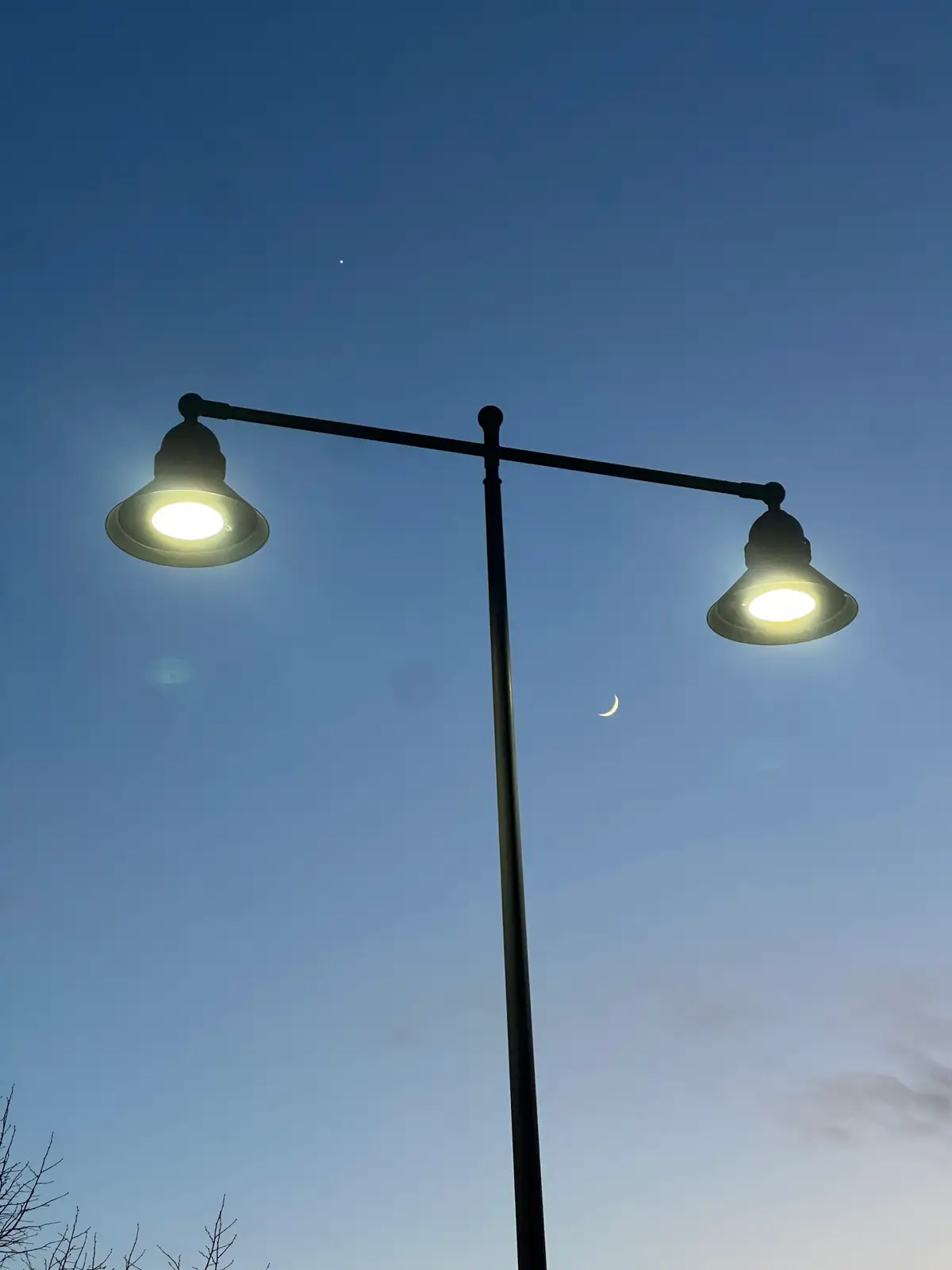 Evening glow, a crescent moon, and city lights illuminate the sky. Still Frame